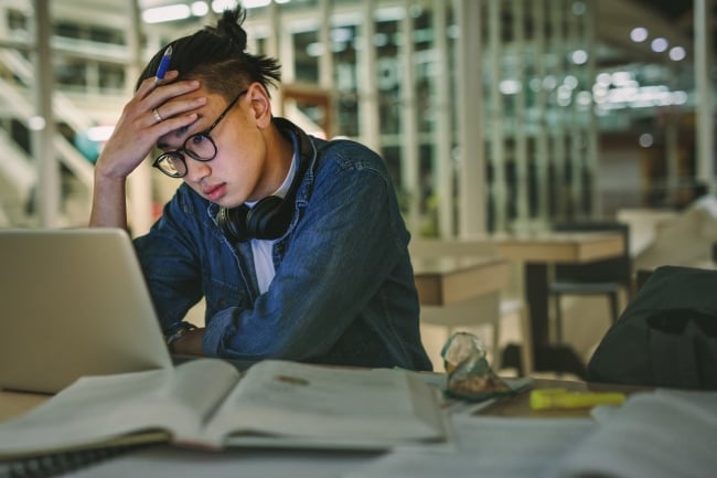 An overwhelmed student sitting in a library staring at his laptop 