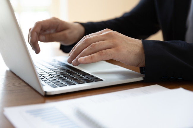 male hands typing on a laptop computer with several pads of paper on the side