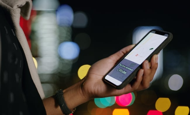 Cropped shot of a woman using a smartphone to order a cab in the city at night