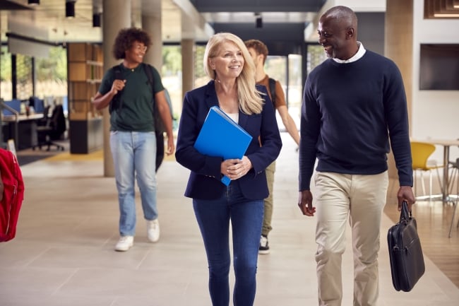 Female and male professor walking and talking animately in busy college or university building with students