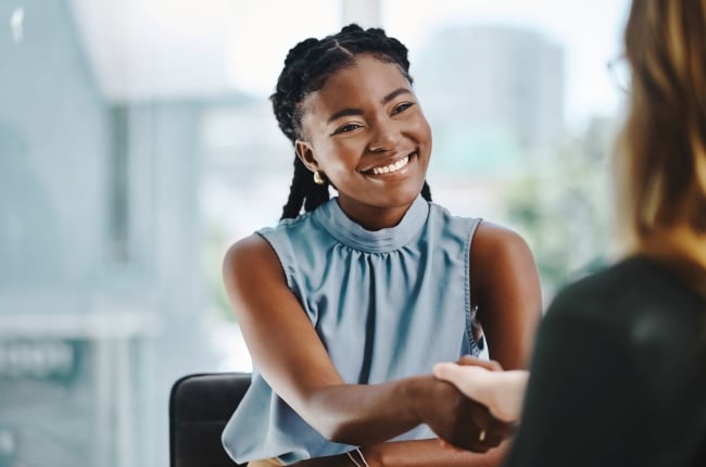 A student in business attire smiles while shaking a woman's hand.