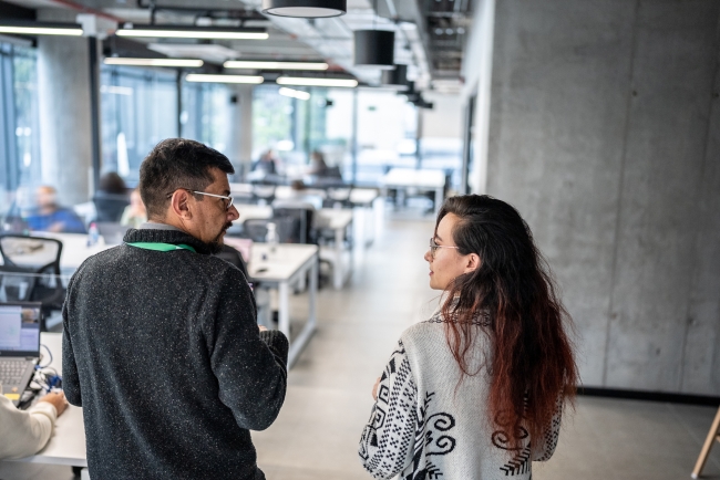 An older professional walks alongside a younger intern through the office