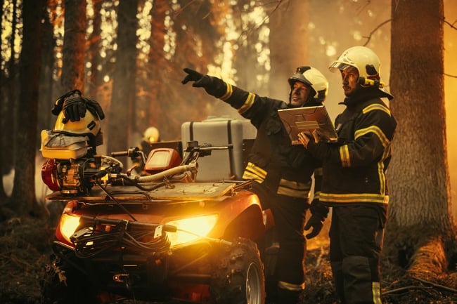 Portrait of two professional firefighters standing next to an all-terrain vehicle, using heavy-duty laptop computer and figuring out a best strategy for extinguishing the wildland fire