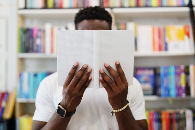 Closeup of a young Black man’s hand holding an open book in a library