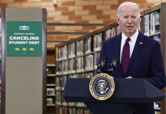 Joe Biden stands at a podium in front of bookshelves and a green sign that says Canceling Student Debt