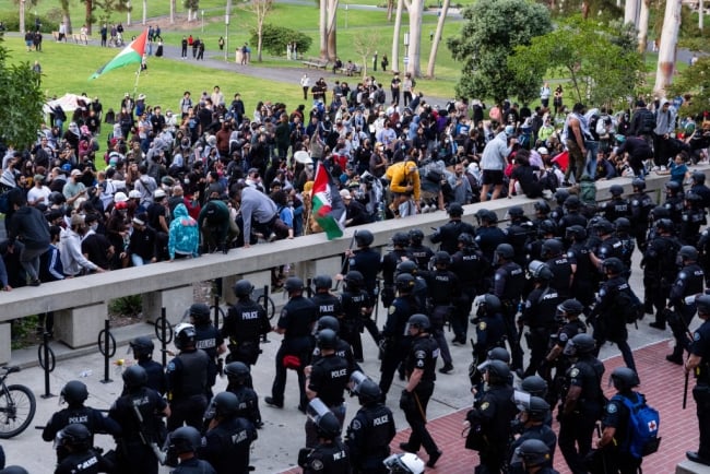 Police officers can be seen moving toward a densely packed group of student protesters on a campus lawn.