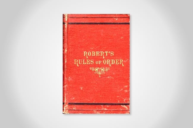 An aged copy of the original Robert's Rules of Order. The cover is red with gold writing.