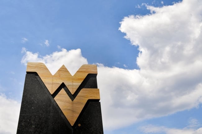 The West Virginia University logo on a monument against a blue sky