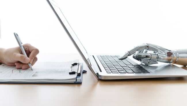 Human hand writing in script while a robot hand types on a laptop