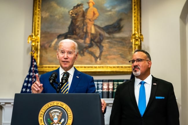 President Biden stands at a podium next to Education Secretary Miguel Cardona