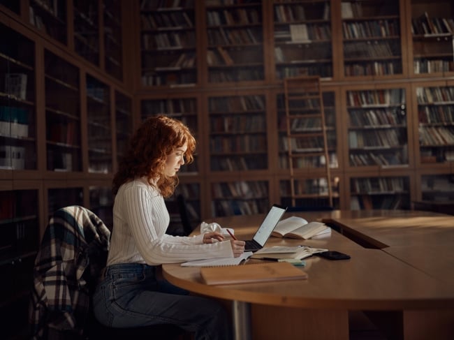 Young woman sits in library writing at a computer 