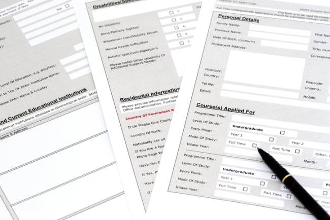 Paper copies of a generic university application form -- three pages are fanned out, with a pen lying on top.