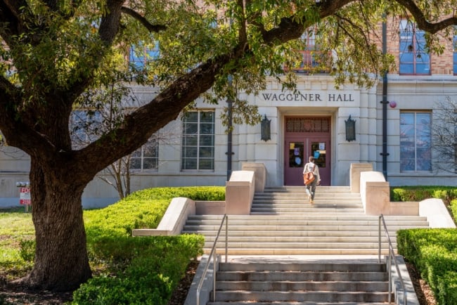 Student walks up stairs to door, under tree