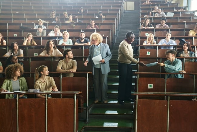 Two instructors give students exam papers during a lecture hall course.