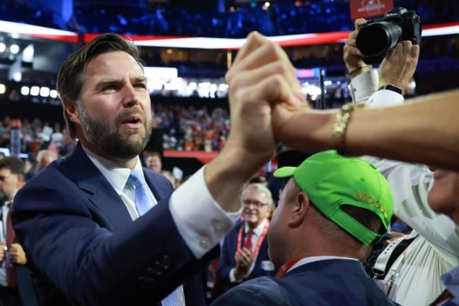 J.D. Vance, in a blue suit, shakes hands with someone on the floor of the Republican National Convention.