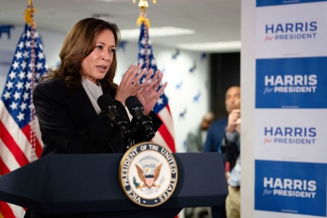 Vice President Kamala Harris stands behind a podium and next to a blue and white poster that says Harris for President