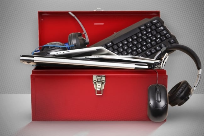 A red toolbox holds technology items including a keyboard, computer mouse and headphones. 