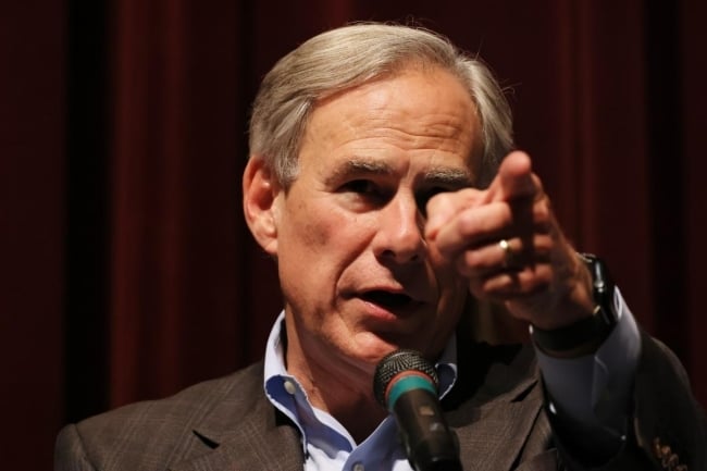A photograph of Texas governor Greg Abbott, behind a microphone, pointing.
