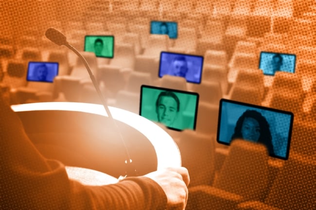 A person stands at a podium and faces several screens that have faces in them, which are placed in a lecture hall