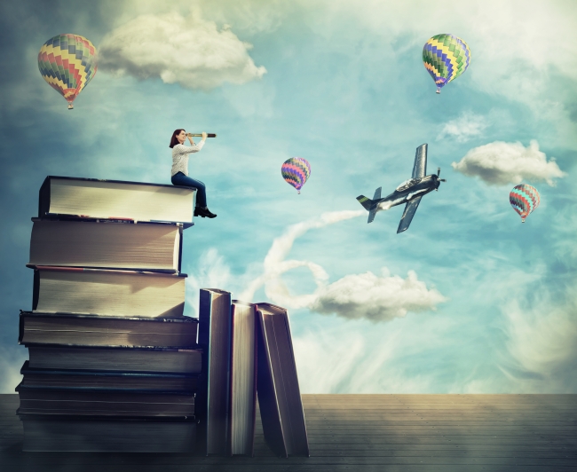 Woman sits atop a high stack of old books looking through a telescope at bright colored flying balloons and an airplane