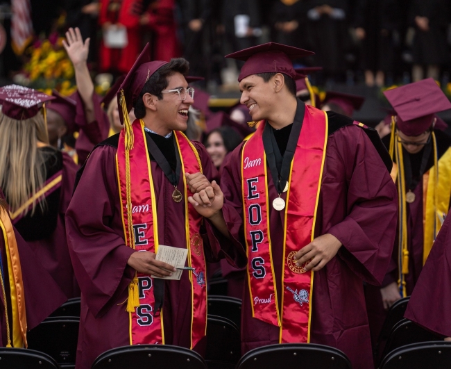 Two graduates of Victor Valley College smile and fist bump at graduation