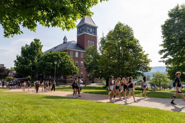 Students walk down a pathway past a building and trees