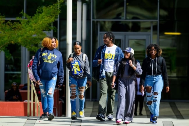 A group of five students, some wearing North Carolina A&T shirts and sweatshirts, walk on campus. 