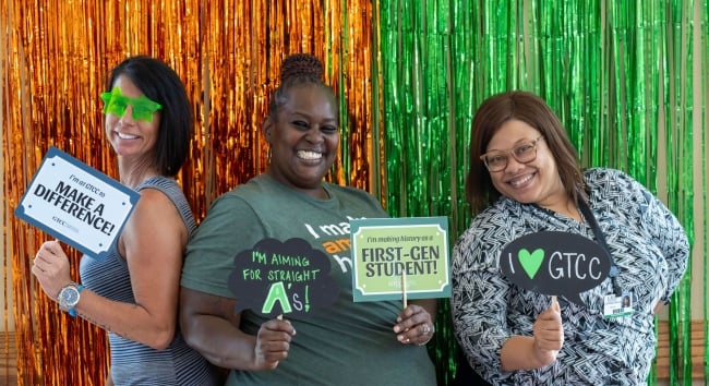 Students pose in a photo booth, holding signs that say "First-gen student," "I make a difference" and "I heart GTCC."