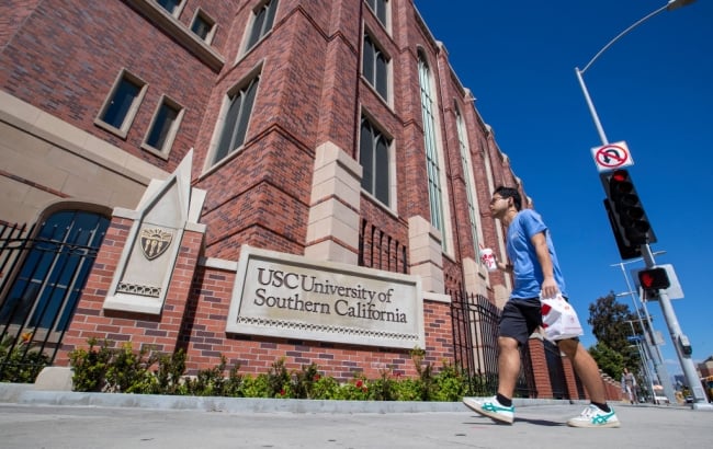 A student in a blue shirt walks past a brick campus building