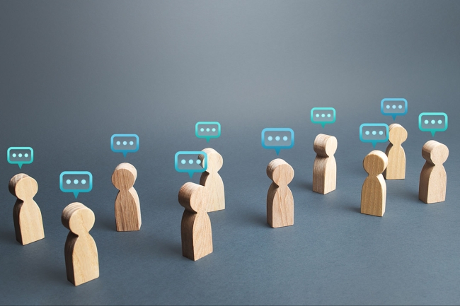 10 miniature wooden people figurines are pictured, each with speech bubbles over their heads, against a dark-gray background.