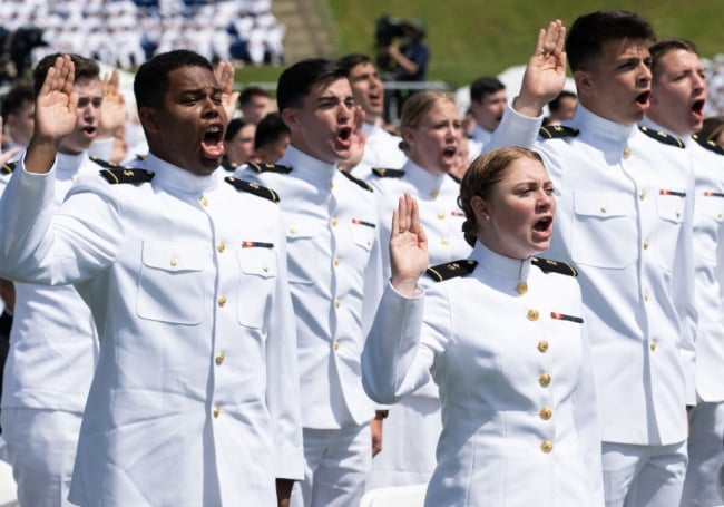 Graduate cadets in white uniforms salute in a crowd