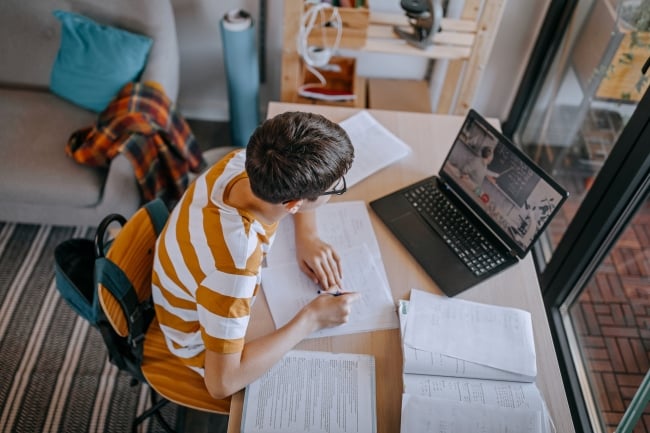 Boy participating in online education training class with teacher using laptop at home