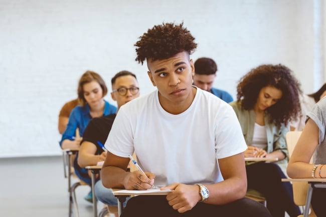 A student of color is looking up in a classroom, possibly confused, as his classmates around him are engaged in work.