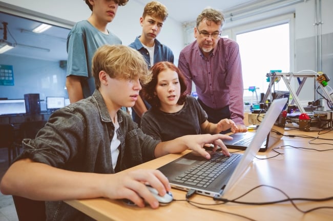 Group of Gen Z teenage high school students and male teacher, using laptop for a programming lessons.