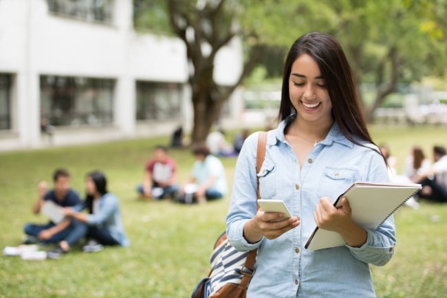 Portrait of a happy Latin American female student texting on her cellphone at the university