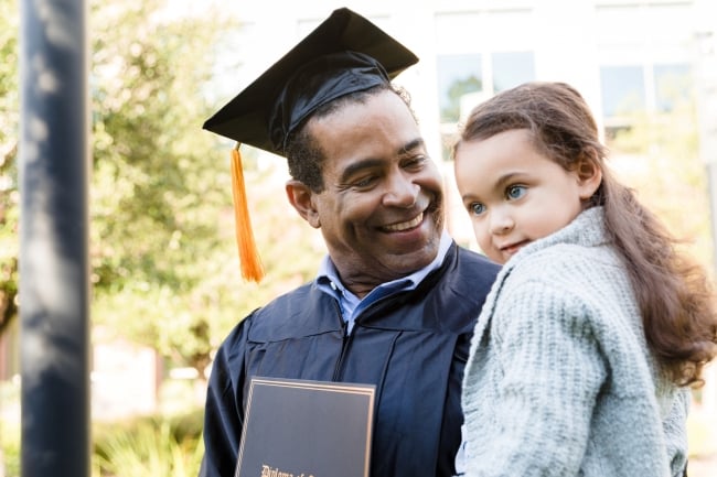 After his graduation ceremony, a man carries a preschool-age child in his arms.