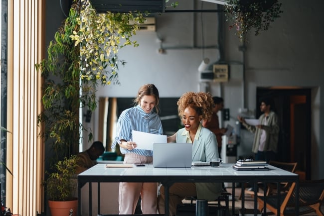 Two women work together in an office, smiling