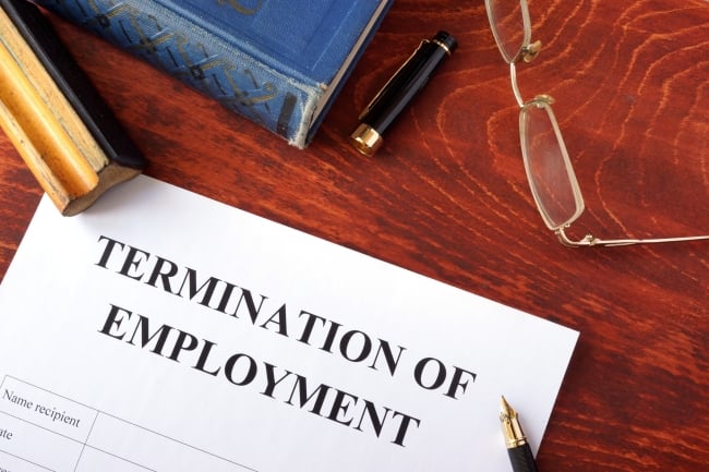 A notice that reads "Termination of Employment" on a desk, next to a book and pair of eyeglasses.