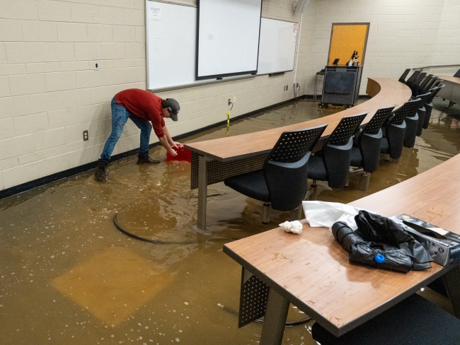 Volunteer scoops floodwater in classroom