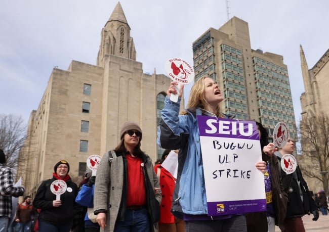 A photograph of demonstrators, with high rises in the background, holding signs supporting the Boston University Graduate Workers Union.