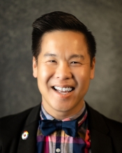 Kevin Nguyen smiles for a headshot wearing a blue bowtie, striped shirt and dark suit coat