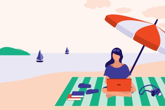 Woman sitting at beach working on computer with several books beside her