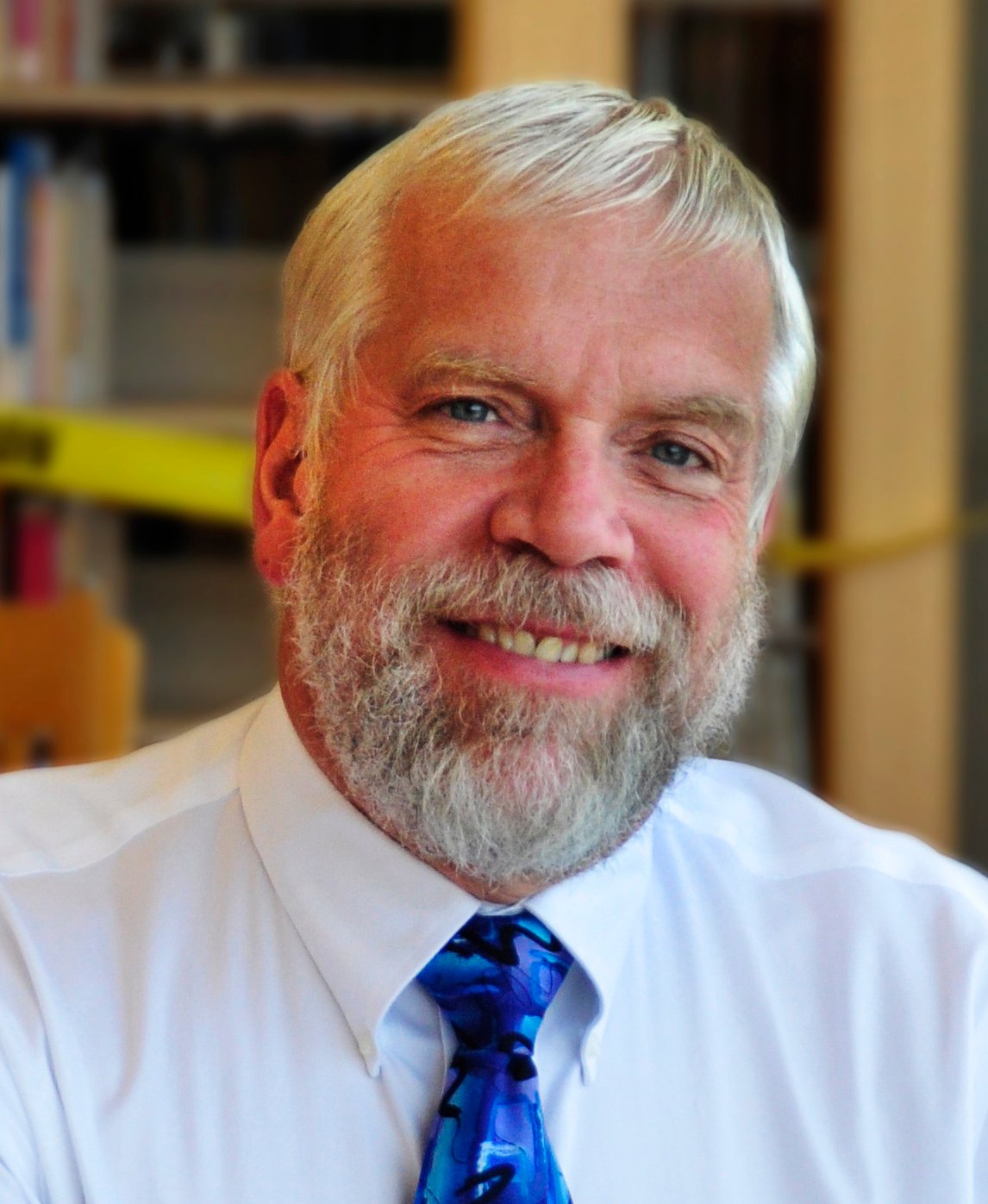 David Lewis, a white man with white hair and a beard wearing a blue necktie.