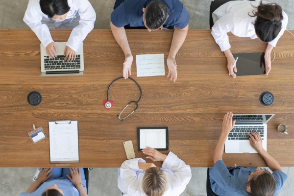 An overhead shot shows a team of medical professionals working on laptops at a shared table.