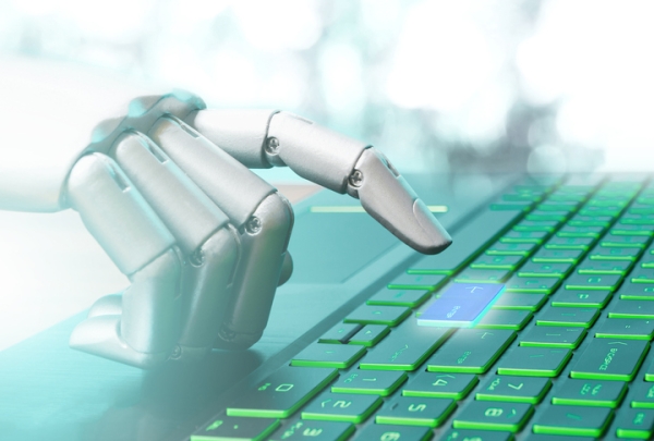 A shiny silver robotic hand types on a laptop keyboard.